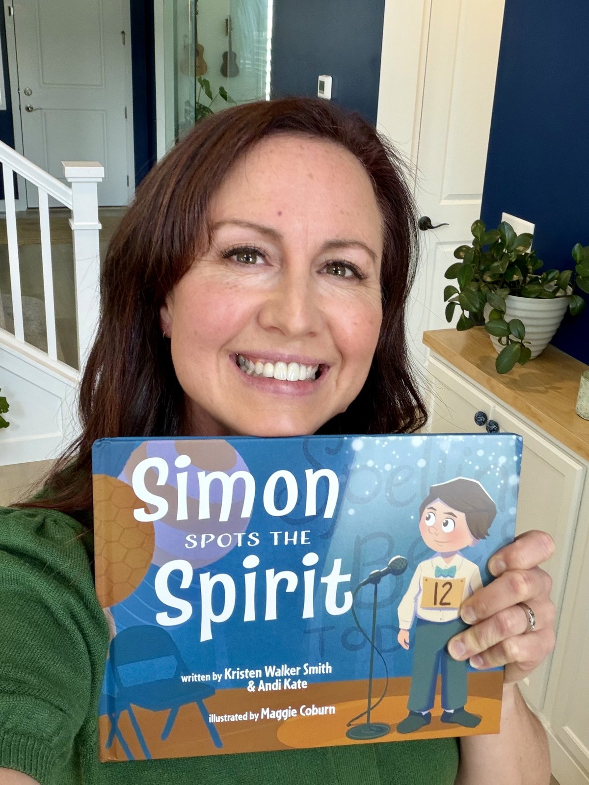 Andi Kate smiling and holding a copy of Simon Spots the Spirit